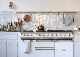 White range wall with copper cookware and pale decorative tile backsplash.