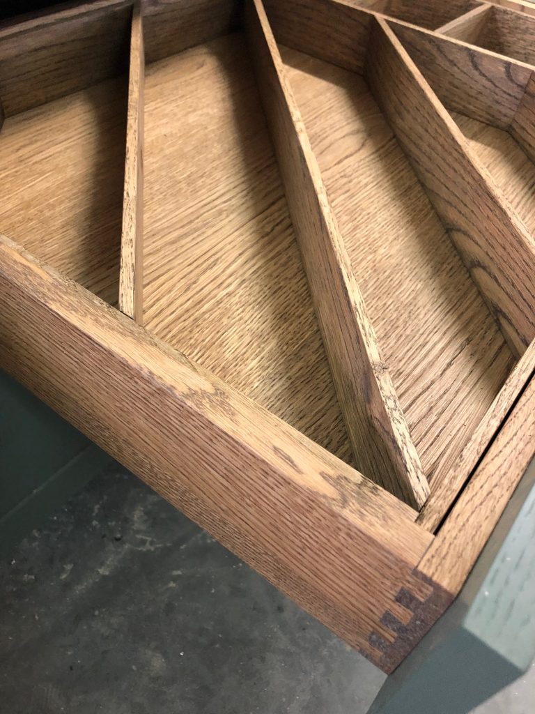 Wood drawer with narrow sloped dividers.