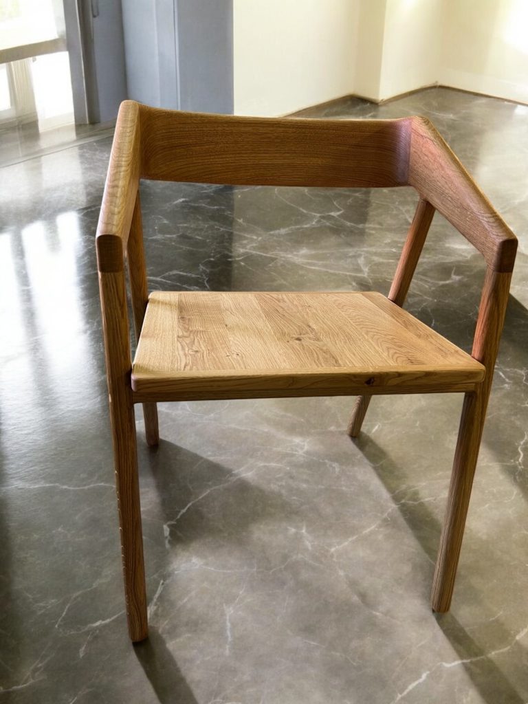 Wooden armchair with broad arms photographed beside a bright window.